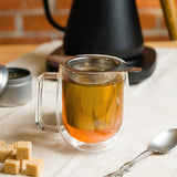 Thé infusé dans une tasse en verre à l'aide du panier infuseur à thé en maille